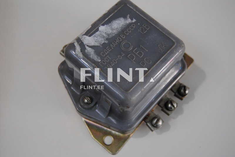 Toode on hall plastmassist klots, millel on kolm metallist ühenduskohtade ja vasakpoolne väljund. Klotsil on tekst ja sümbolid, sealhulgas 'RB1' ja '12V'.