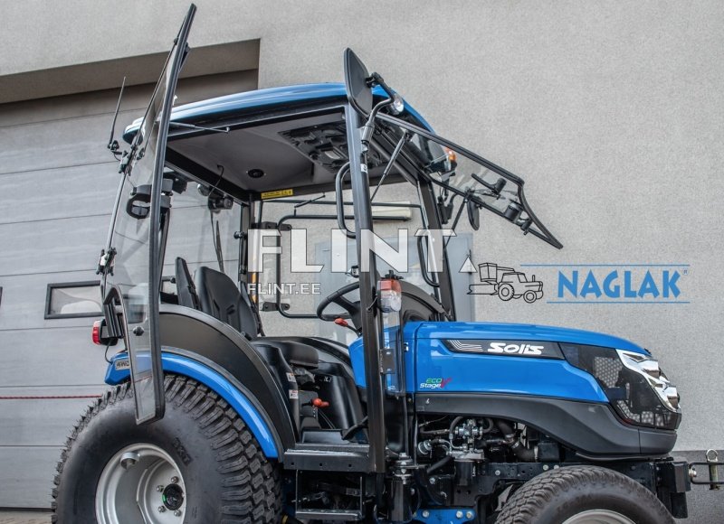 Traktor, millel on sinine kere ja avatud juhi kabiin. Kabiini külgedel on klaassuunajad ja avatud uks, mille kaudu on näha istet ja juhtseadmeid.