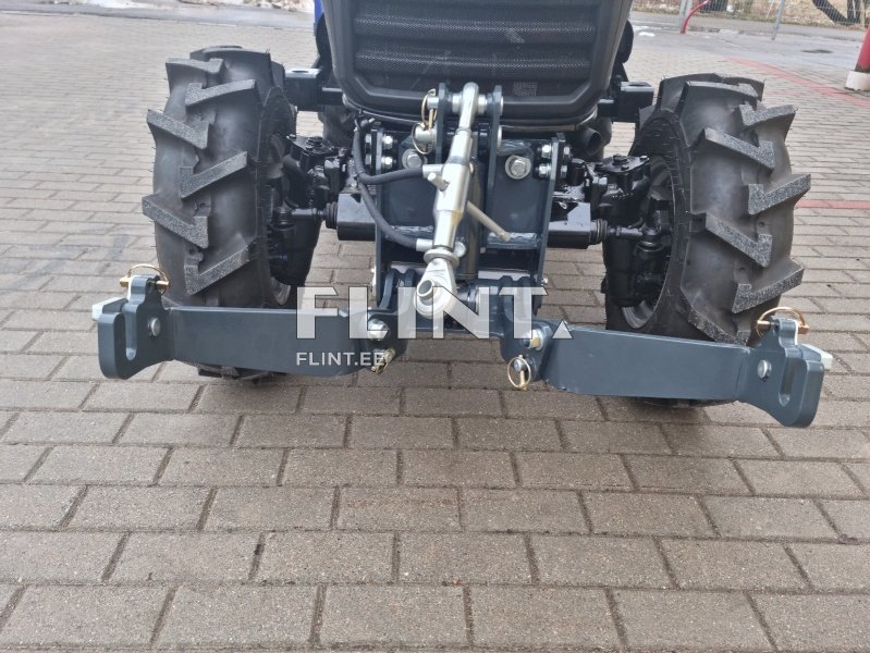 Traktor, millel on mustad rehvid ja metallist haakeseade, on paigutatud sillutatud teele.